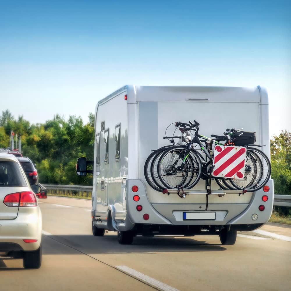 Camper with reflective oversized load sign and bicycles on a highway, showcasing durable polycarbonate reflective board.