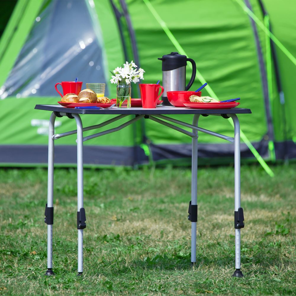 Подарък за човек, който обича къмпинг: сгъваема маса за къмпинг на зелена поляна с чинийки и чаши.