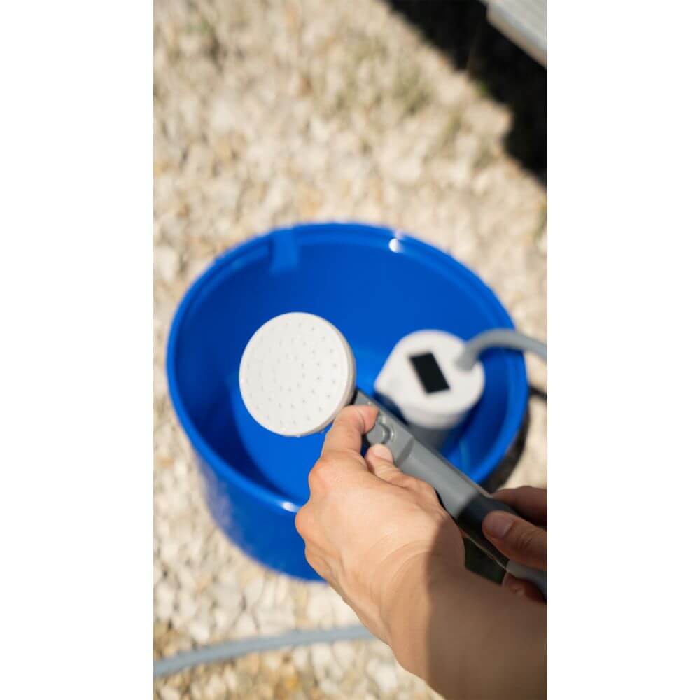 Person holding portable shower head with rechargeable battery, next to a blue bucket, ideal for camping and outdoor activities.