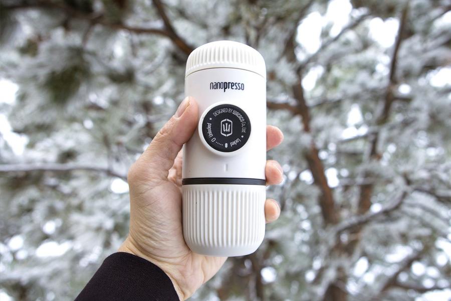 Преносима ръчна машина за кафе еспресо Wacaco Nanopresso в ръка на фон със сняг.