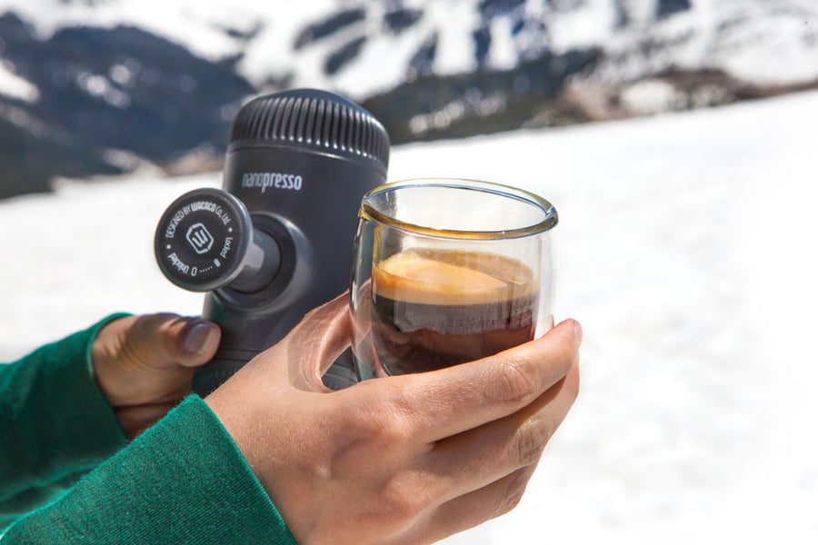 Преносима ръчна машина за кафе Wacaco Nanopresso, човек държи чаша с еспресо на фона на снежни планини.