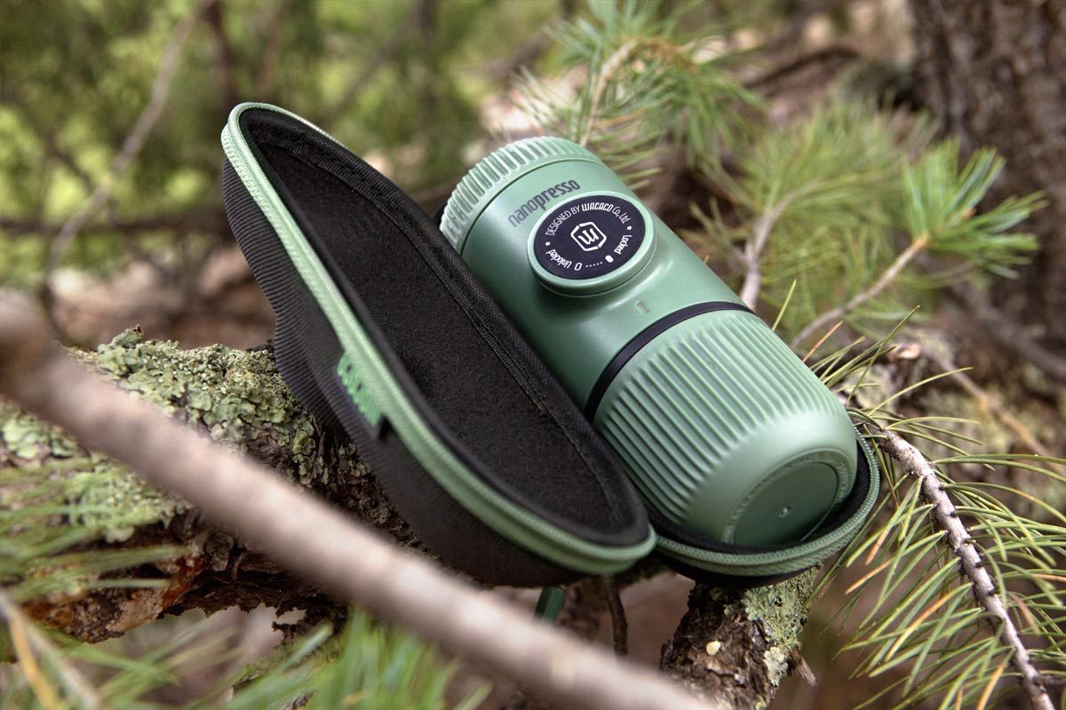 Преносима ръчна машина за кафе Wacaco® Nanopresso в зелена чанта, разположена сред дървета.