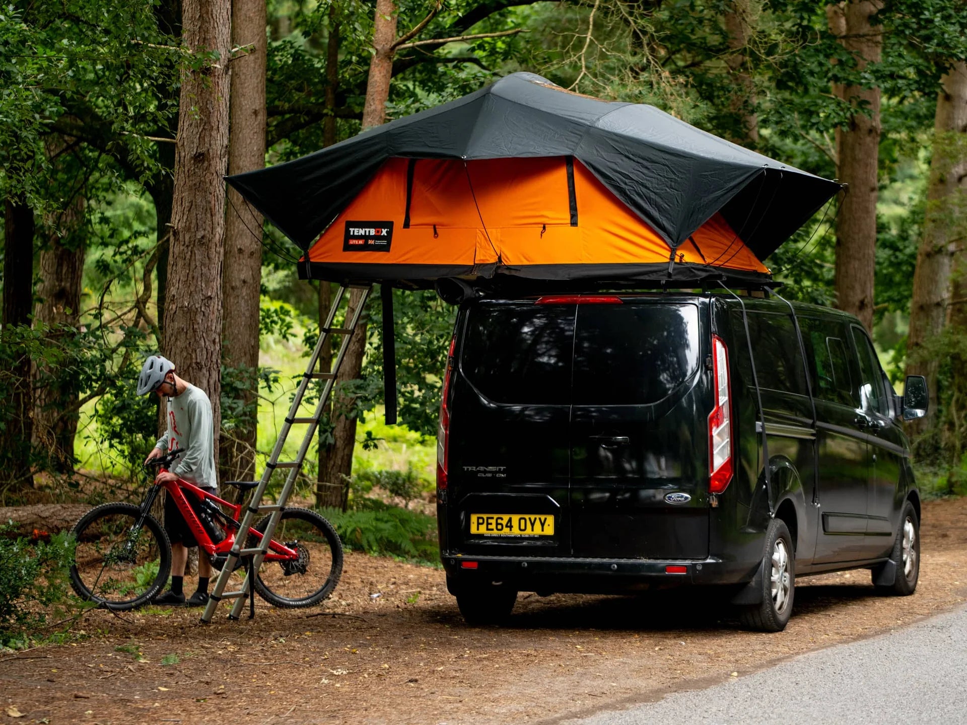 TentBox Lite XL – Покривна палатка за 4-ма, инсталирана на автомобил с стълба, в гориста местност.