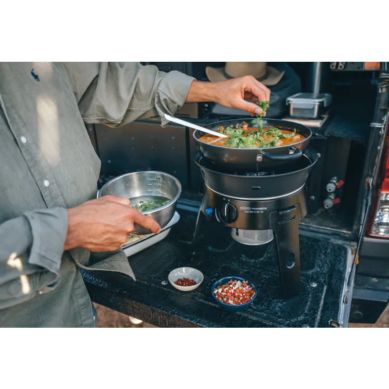 Приготвяне на храна на преносимо газово барбекю CADAC Safari Chef 30 LP Deluxe по време на къмпинг.