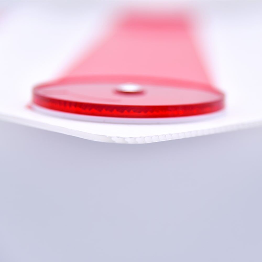 Close-up of a durable red reflector tab on a white polycarbonate surface, part of an oversized load warning sign for campers and caravans.