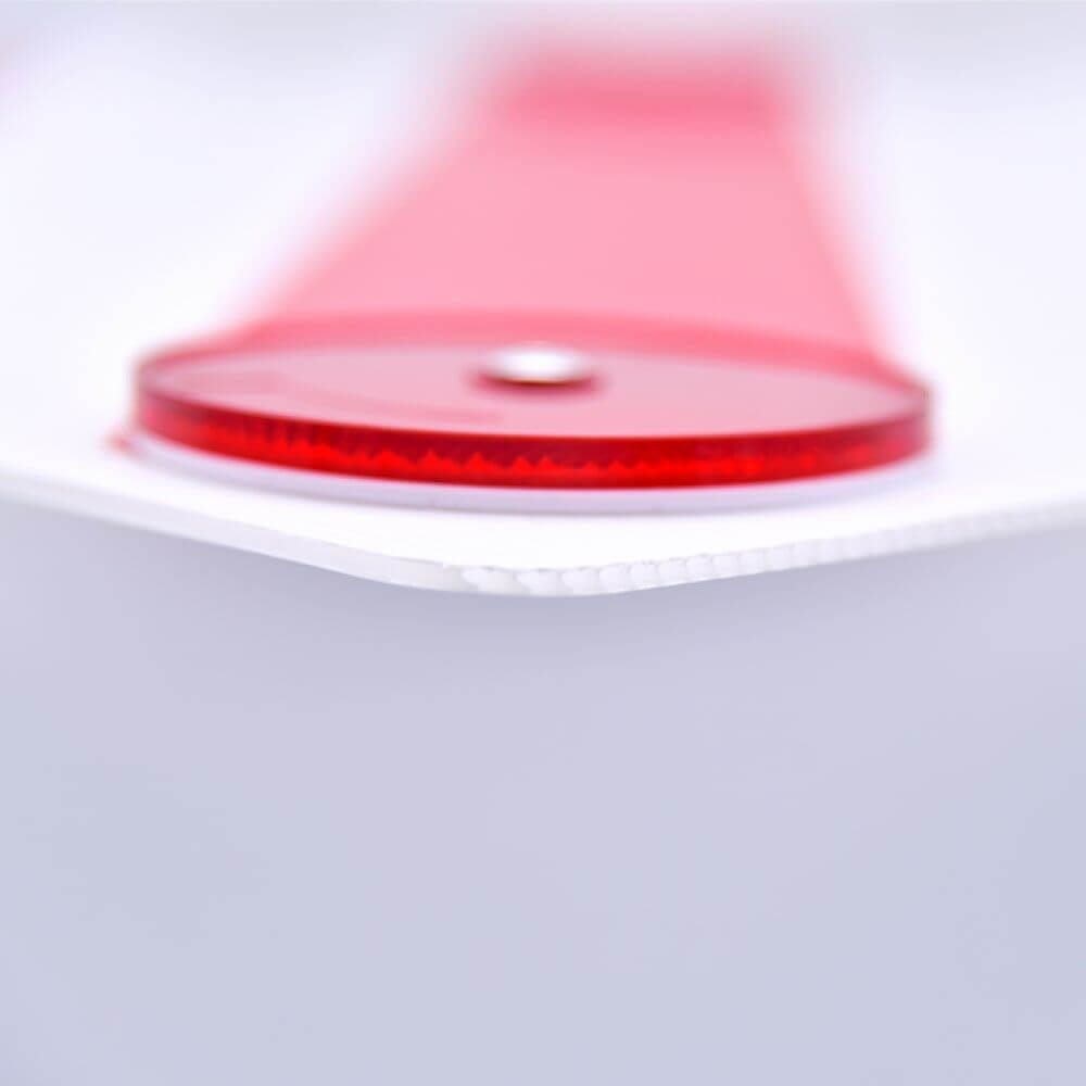 Close-up of a durable red reflector tab on a white polycarbonate surface, part of an oversized load warning sign for campers and caravans.