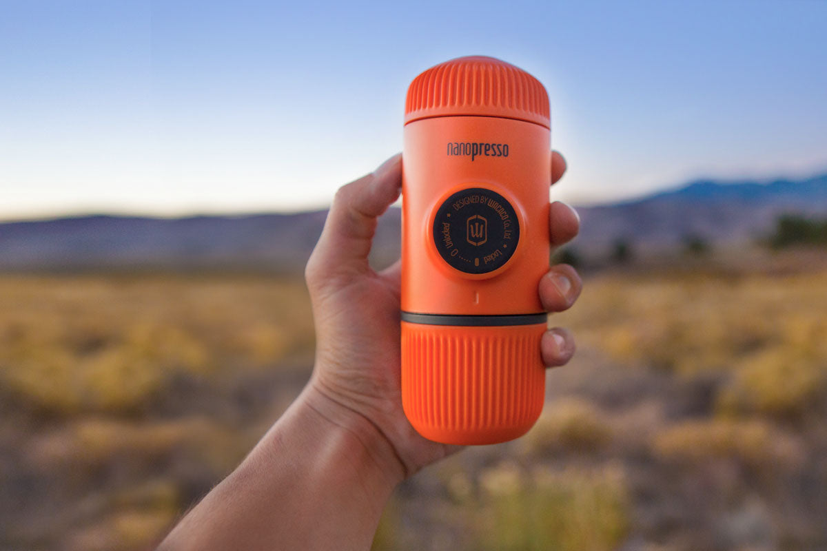 Преносима ръчна машина за кафе Wacaco Nanopresso в ръка на фона на природа за къмпинг.